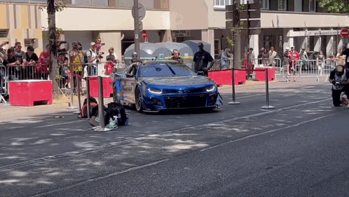Blue Car Driving Down Street with Crowd