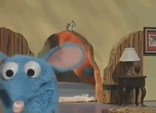 Blue Stuffed Animal Standing Next to Bed and Lamp