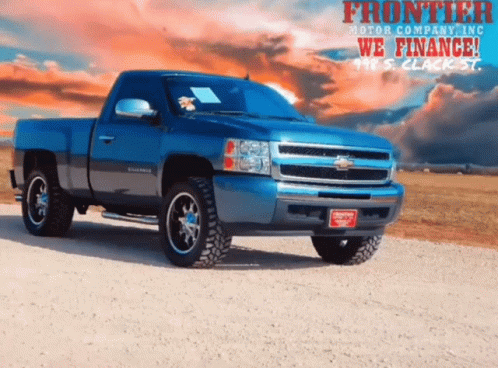 Blue Truck Parked On Dirt Road In Front Of Frontier Motor Company Ad GIF