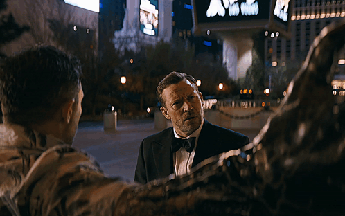 Blurry Man In Tuxedo Walking Past Sign Saying A GIF