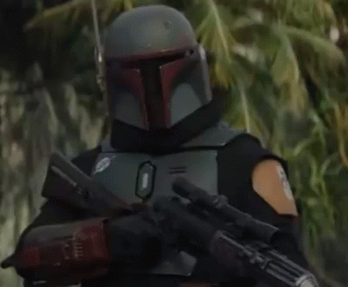 Boba Fett Is Wearing A Helmet And Holding A Gun In A Forest . GIF