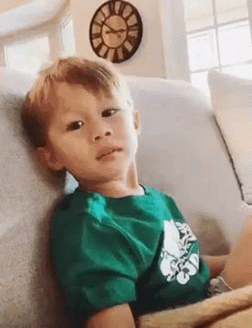 Boy in Green Shirt Sitting on Couch With Clock