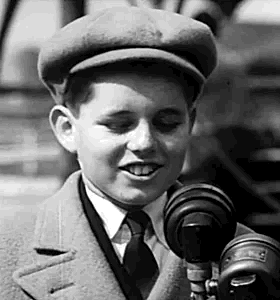 Boy in Hat and Tie Talking Into Microphone
