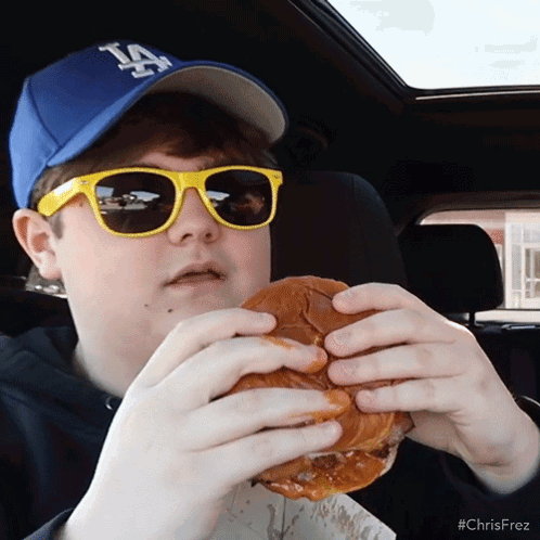 Boy in LA Hat and Sunglasses Eating Hamburger