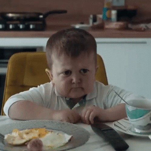 Boy Sitting At Table With Food And Remote GIF