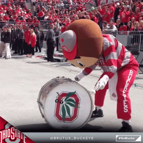 Brutus Buckeye Mascot Playing A Drum In Front Of A Crowd Of People GIF