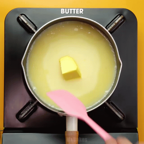 Butter Is Being Stirred In A Pot With A Pink Spatula GIF