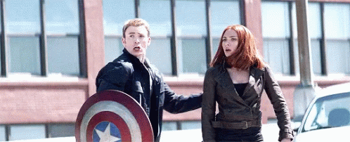 captain america and black widow are standing next to each other on the street .