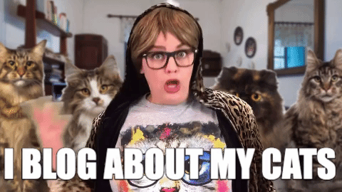 Cat Lady With Pictures Of Pets Behind Her GIF