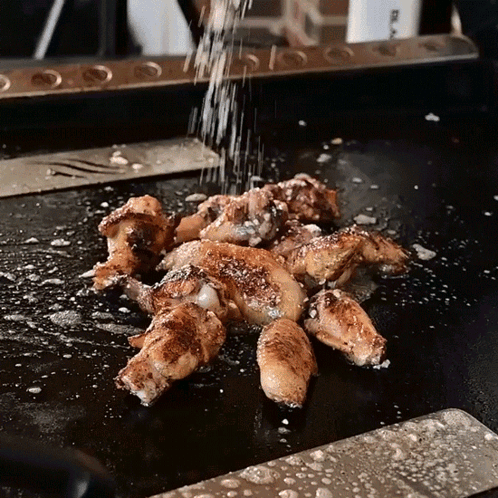Chicken Wings Are Being Sprinkled With Salt On A Griddle GIF
