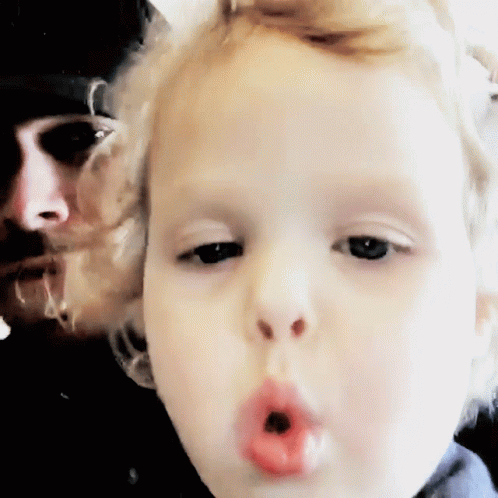 Child Blowing Kiss With Man In Background GIF