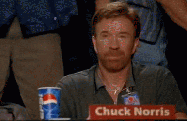 Chuck Norris Is Sitting At A Table With A Sign That Says Chuck Norris On It . GIF