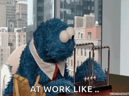 Cookie Monster Sitting at Desk with Newton's Cradle