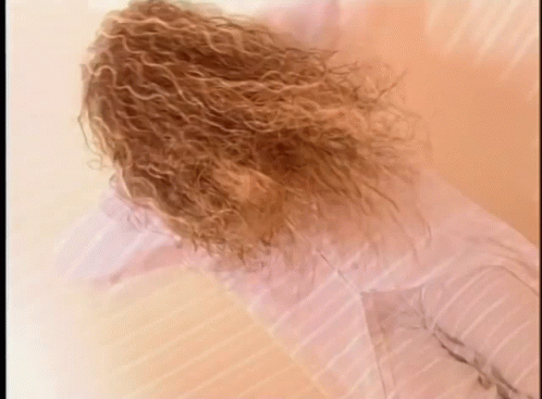 Curly Hair Woman Laying On Bed In White Shirt GIF