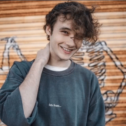 Curly Haired Man Smiling Next to Skeleton Wall