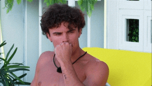 Curly-Haired Shirtless Man Covering Nose on Yellow Couch