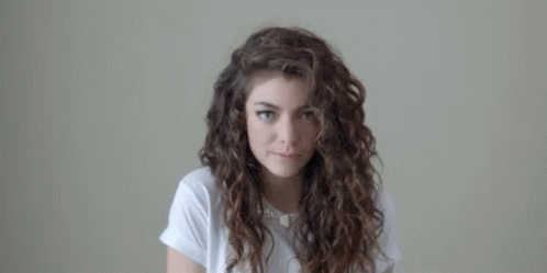 Curly-Haired Woman In White Shirt Looking At Camera GIF