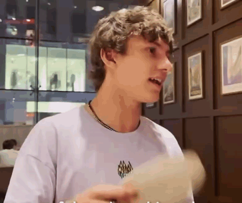 Curly Haired Young Man Holding Paper By Picture Wall