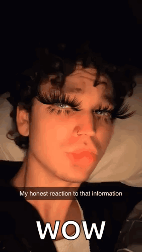 Curly-Haired Young Man With Fake Eyelashes on Bed Says Wow