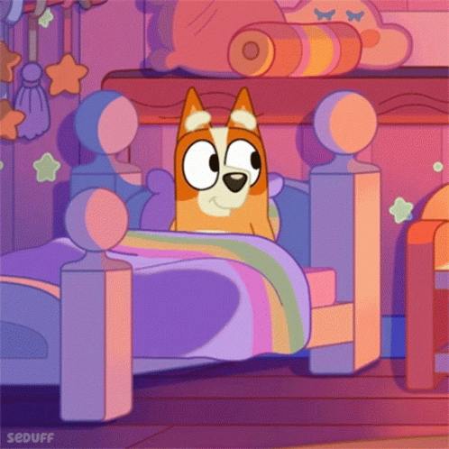 Dog Lying In Bed With Rainbow Blanket GIF