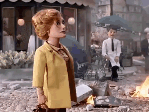 Doll in Yellow Coat in Front of Burning Building