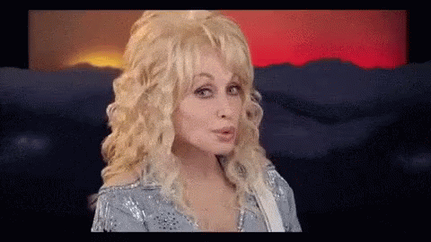 Dolly Parton Making Funny Face Holding Guitar in Front of Mountains