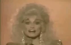 Dolly Parton Singing Into Microphone in Front of Pink Wall