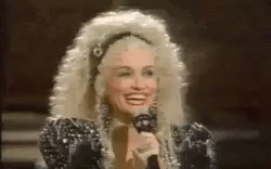 Dolly Parton Smiling Holding Microphone in Wig