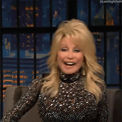 Dolly Parton Smiling in Chair in Front of City Skyline