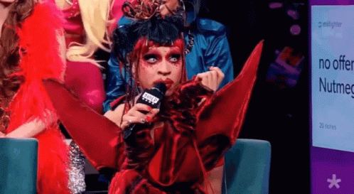 Drag Queen Holding Microphone in Front of Nutmeg Sign