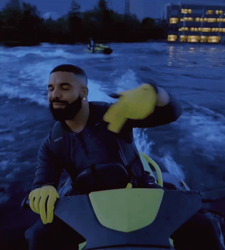 Drake Is Riding A Jet Ski In The Water With A Yellow Glove On GIF