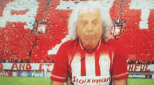 Elderly Man in Stoiximan Shirt in Front of Crowd