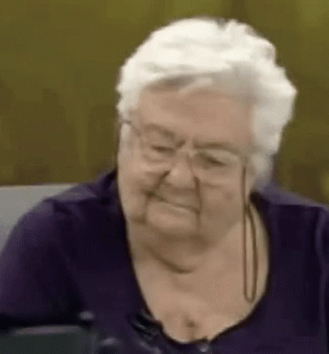 Elderly Woman in Glasses and Purple Shirt Smiling on Couch