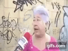 Elderly Woman Talking Into Microphone in Front of Graffiti Wall