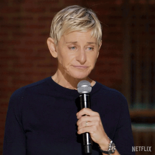Ellen Degeneres Is Holding A Microphone In Front Of A Brick Wall With Netflix Written On The Bottom Right GIF