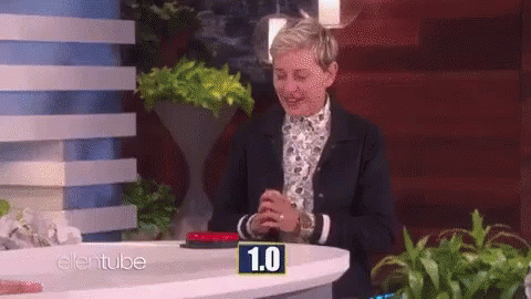 Ellen Degeneres Is Sitting At A Table With A Button That Says 1.0 On It GIF