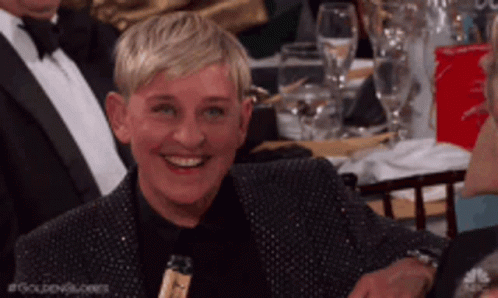 Ellen Degeneres Is Smiling While Sitting At A Table GIF