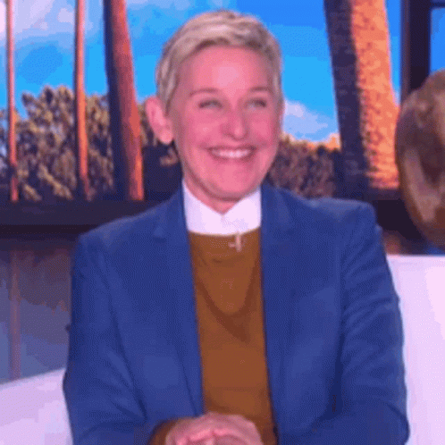 Ellen Degeneres Is Smiling While Sitting On A Couch In Front Of A Window . GIF