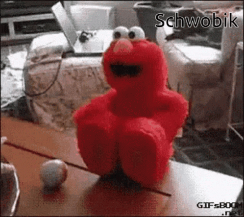 Elmo From Sesame Street Is Sitting On A Table With A Ball GIF