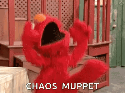 Elmo From Sesame Street Is Standing In Front Of A Table With His Mouth Open And Says `` Chaos Muppet '' . GIF