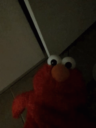 Elmo From Sesame Street Is Standing In The Corner Of A Dark Room GIF