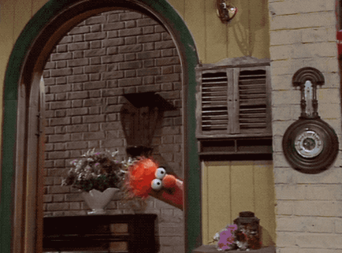 Elmo From Sesame Street Looks Out A Window With A Vase Of Flowers GIF