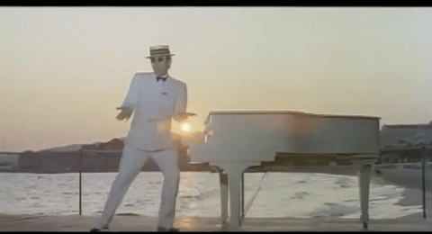 Elton John Standing Beside White Piano GIF