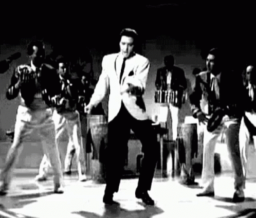 Elvis Presley Is Dancing On A Stage In A Black And White Photo With A Band Behind Him . GIF