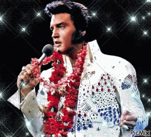 Elvis Presley Singing Into A Microphone While Wearing A Red Flower Lei Around His Neck GIF