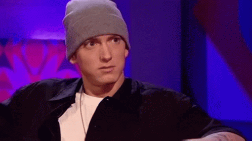 Eminem Is Wearing A Beanie And A Black Shirt While Sitting In A Chair . GIF