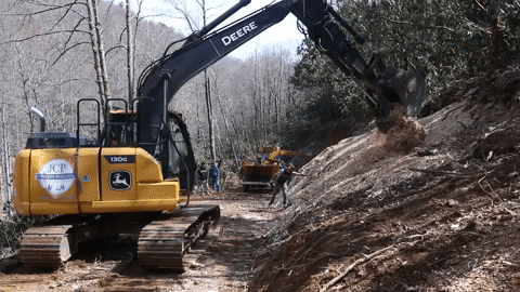 Excavator Spreading Mulch At Bottom Of Mountain GIF