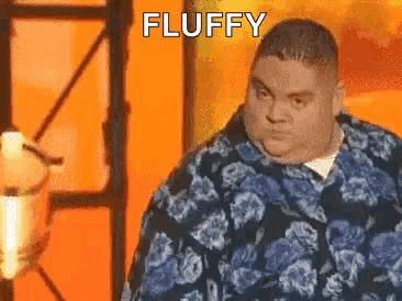 Fat Man in Blue Floral Shirt in Front of Orange Wall Saying Fluffy