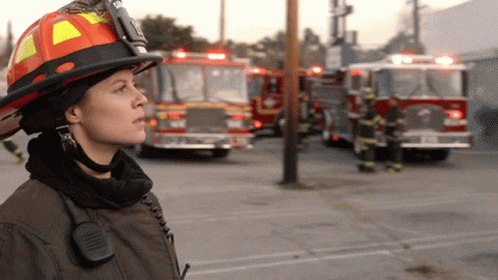 Female Firefighter With Helmet And Walkie Talkie In Front Of Fire Trucks GIF