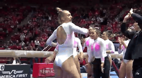 Female Gymnasts on Balance Beam in Front of Crowd